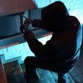 Dunkle Umgebung. Ein Einbrecher versucht ein Kellerfenster zu öffnen. Er trägt schwarze Kleidung und Kapuze. 