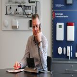 Ein Berater sitzt vor einer Beratungskulisse und hält ein Telefon in der Hand. 