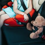 Kleinkind, angeschnallt im Kindersitz im Auto. Daneben ein Teddy, ebenfalls angeschnallt.