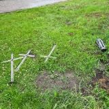 Drei Kreuze aus Metall und ein Grablicht liegen auf einem Rasenstück