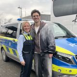 Der Sänger Kamrad steht neben einer Polizistin und beide lächeln in die Kamera.