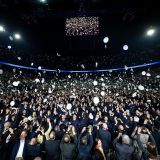 Bei der Vereidigungsfeier in der Lanxess Arena in Köln werfen dreitausend Polizeianwärterinnen und -anwärter ihre Dienstmützen feierlich in die Luft. Sie tragen Uniform. Im Hintergrund ist es dunkel. Ein großer Bildschirm überträgt die Szene für das Publikum.