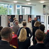 Das Bild zeigt Besuchende der Ausstellung inmitten der Exponate, in der Mitte steht Moderator Ralf Hövelmann