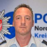 Bezirksdienstbeamter Oliver Pfeiler vor Leinwand mit dem Logo der Polizei Düren