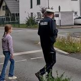 Ein Polizist und ein Mädchen üben den sicheren Weg zur Schule und gehen über eine Fußgängerampel. Text: Kreis Gütersloh. Schulstart 2025 - Rechtzeitig den Schulweg üben