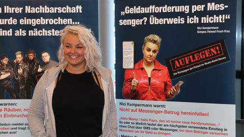 Nici Kempermann steht vor ihrem Plakat und warnt: "Geldforderungen per Messenger? Überweise ich nicht""