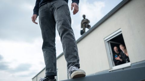 A suicide situation is simulated during training. A man is standing on the edge of a roof. In a window behind him, members of the negotiation team can be seen talking to the man. On a higher roof in the background stands a SEK security shooter.