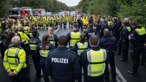 Eine Gruppe von Polizei- und Feuerwehrkräften steht nach einer Verkehrsunfallübung gemeinsam im Kreis auf einer gesperrten Autobahn. Eine Person spricht in die Menge. Im Hintergrund sind mehrere Polizei- und Feuerwehrfahrzeuge zu sehen.
