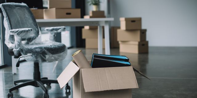 Ein neuer Bürostuhl in Folie verpackt und Kartons mit Akten in einem Büro