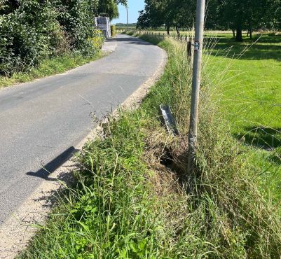 entlang eines asphaltierten Feldwegs, führt parallel ein Grünstreifen. In diesem wurde ein silberne Zaunpfahl sowie ein grauer Pfosten eines Verkehrsschilds, beschädigt.