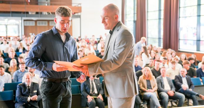 Polizeipräsident Tim Frommeyer überreicht einem neuen Kommissaranwärter seine Ernennungsurkunde in der Aula des Max-Planck Gymnasiums in Gelsenkirchen. Foto: Polizei Gelsenkirchen